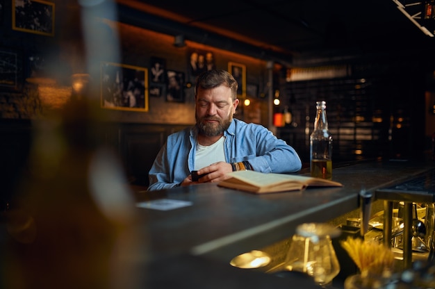 Man using mobile phone at the counter in bar. One male person resting in pub, human emotions, leisure activity, nightlife