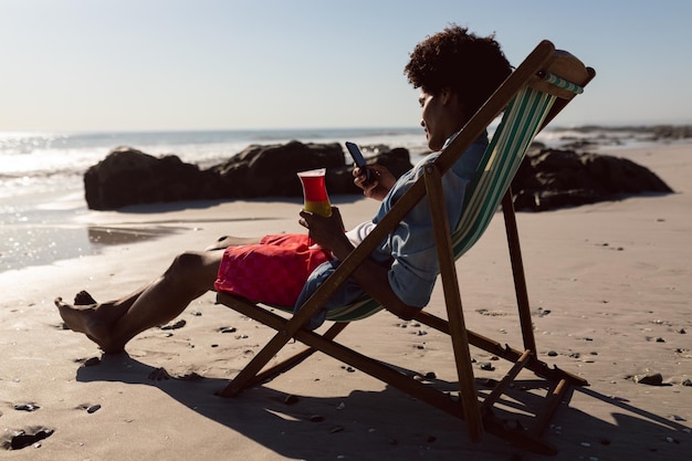Photo man using mobile phone while having cocktail in a beach chair