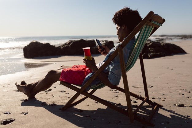 Man using mobile phone while having cocktail in a beach chair