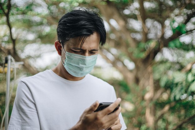 man using mobile phone while wearing mask against trees