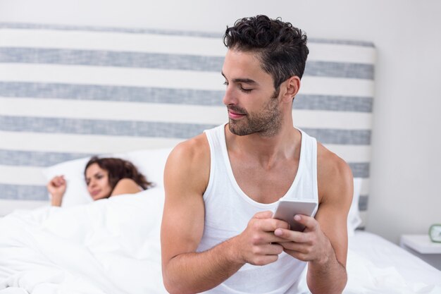 Photo man using mobile phone while wife sleeping on bed