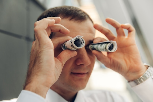 Man using money like binoculars. the man twisted the money with a straw near his eyes.