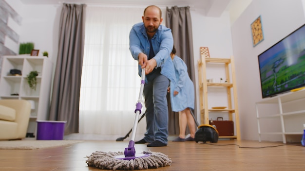 Man using mop to clean the dust from living room floor.