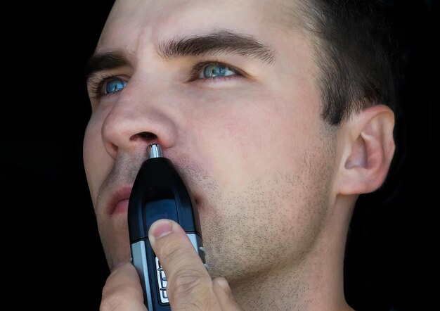 鼻毛トリマーを使用している男性男性は、孤立した黒い背景の鼻から髪を削除します