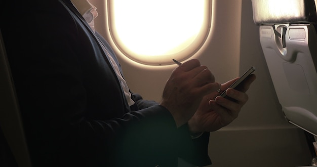 飛行機の中でスマートフォンを入力するためにペンを使用して男