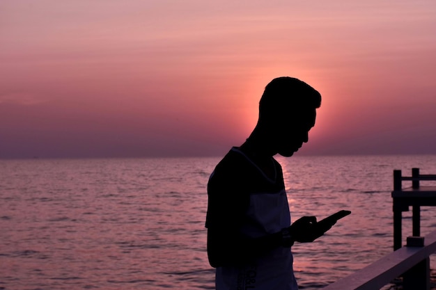 夕暮れ中に海で電話を使っている男性