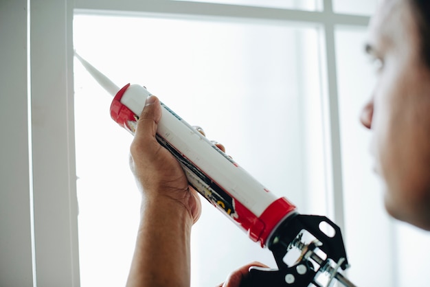 Man using a silicone gun to repair a window