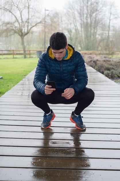 Photo man using smart phone while crouching on wet boardwalk