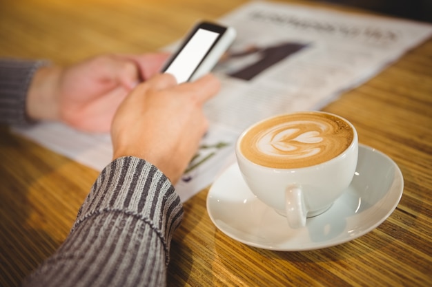 スマートフォンを使って、カプチーノを飲む男