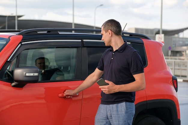 Man using smartphone holding in hand near the car about in the parking lot