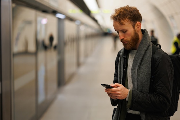 電車を待っている間に地下鉄駅のプラットホームでスマートフォンを使用している男性