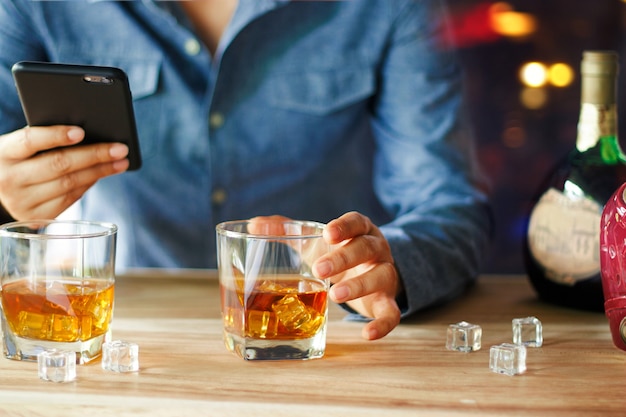 バーカウンターでウイスキーアルコール飲料を飲みながらスマートフォンを使用している人
