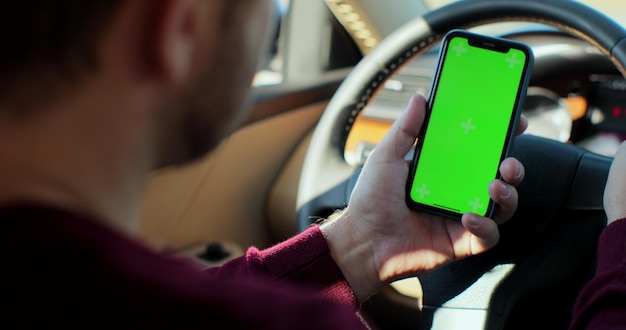 Man using smartphone with green screen chroma key inside car. Concept: direction of travel, address search, message, location, business. Back view.