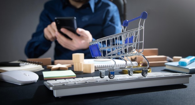 Man using smartphone with a shopping cart on the computer keyboard Online shopping