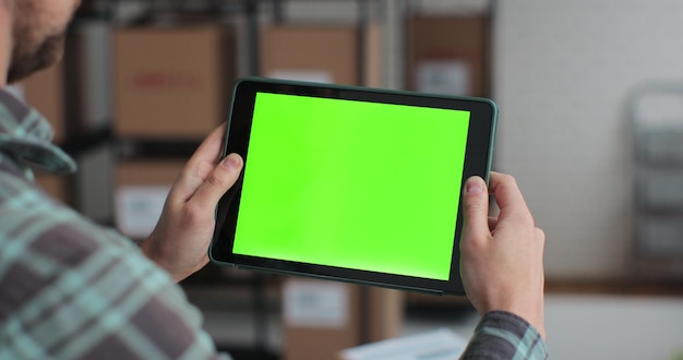녹색 스크린 크로마키가 있는 태블릿 컴퓨터를 사용하는 남자 마분지 상자로 가득 찬 창고에서 인터넷 검색