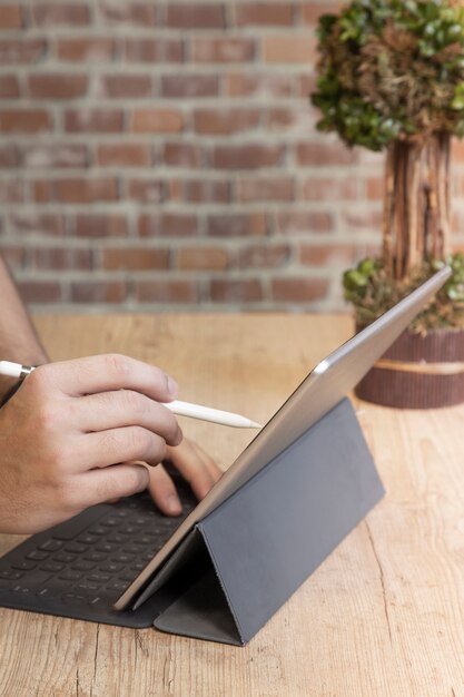 Foto uomo che utilizza un computer tablet per lavorare, su un tavolo di legno, davanti a un muro di mattoni