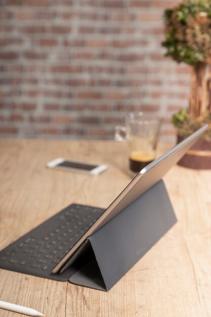 벽돌 벽 앞에 커피 한잔과 함께 나무 테이블에서 작업하기 위해 태블릿 컴퓨터를 사용하는 사람