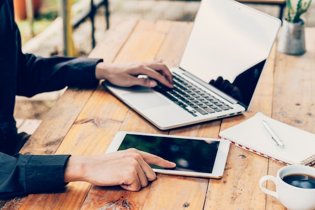 Man using tablet and laptop on table in coffee shop.