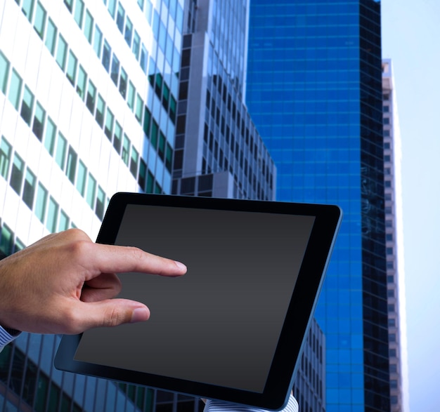 man using tablet pc  against low angle view of skyscrapers