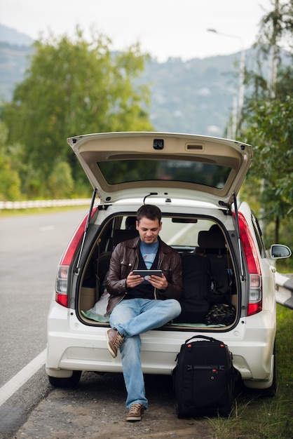 Man using tablet while sitting on the trunk of a car