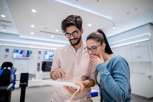 Man using tablet while woman with amazed facial expression looking at it.