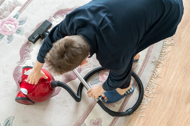 A man using a vacuum cleaner to clean the carpet at home