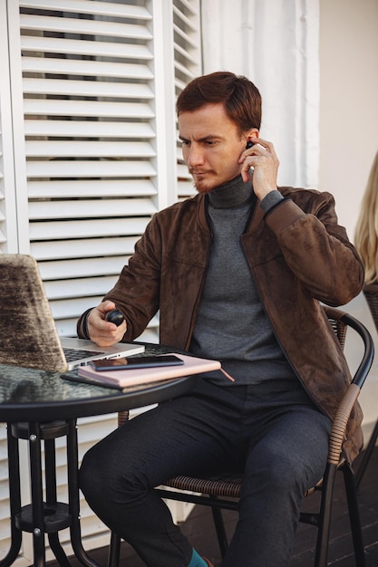 Man using wireless earphones and preparing for video call online via laptop in street cafe