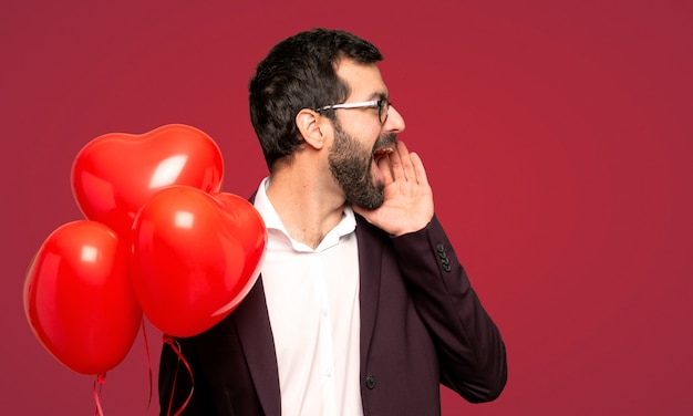 Man in valentine day shouting with mouth wide open to the lateral over red background