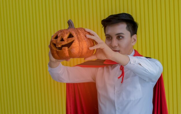 Photo man in vampire costume holding jack o lantern against yellow wall