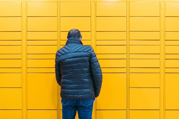 Man van achteren scant een code op de mobiele telefoon om een pakket op te halen uit de gele locker. Messaging concept, vergelijk online, e-commerce en pakketten