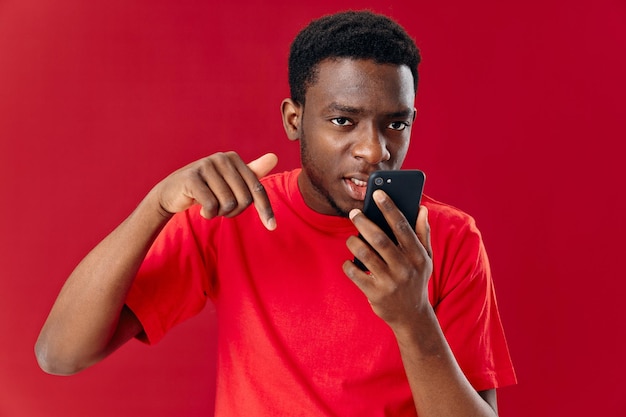 Man van afrikaans uiterlijk in een rode t-shirt met een telefoon in de handen van communicatietechnologie