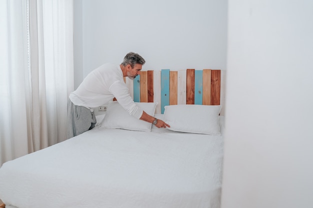 Man van in de 50 met grijs haar bed opmaken
