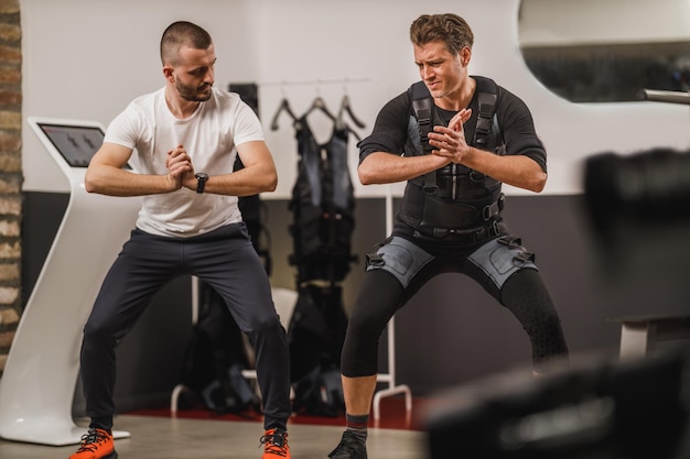 Man van middelbare leeftijd doet EMS trainen met personal trainer in de sportschool.