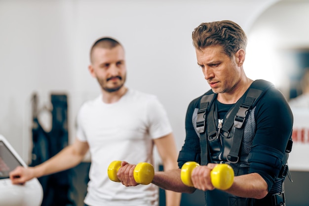 Foto man van middelbare leeftijd doet ems-training met coach in de sportschool.