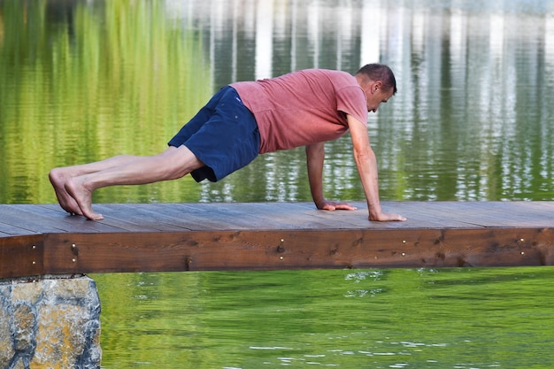 man van middelbare leeftijd doet yoga asana's. mannelijke atleet traint op pier buiten park.