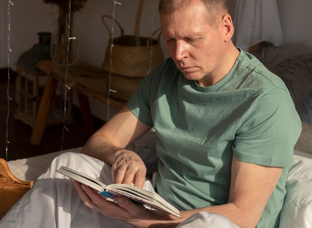 Man van middelbare leeftijd leesboek in gezellig huis, daglicht.