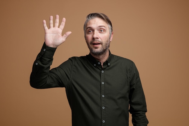 Man van middelbare leeftijd met grijs haar in een donker gekleurd hemd opzij kijkend glimlachend vriendelijk zwaaiend met een handgebaar dat over een bruine achtergrond staat