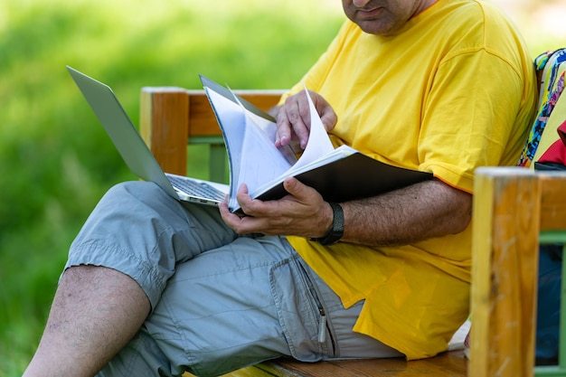 Man van middelbare leeftijd met laptop en documenten die buiten werken in een groen thuiskantoorconcept in de tuin