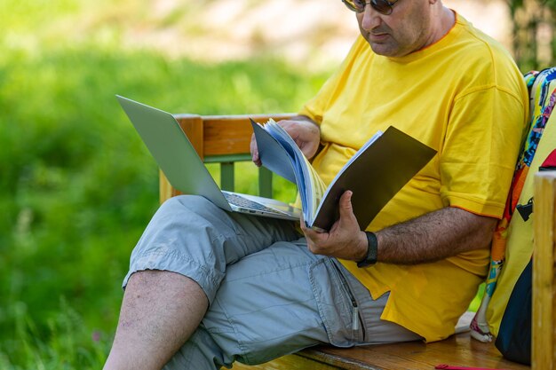 Man van middelbare leeftijd met laptop en documenten die buiten werken in een groen thuiskantoorconcept in de tuin