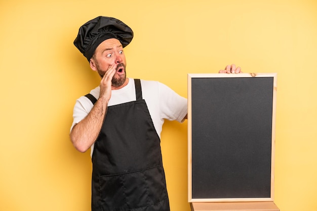 man van middelbare leeftijd voelt zich gelukkig, opgewonden en verrast. chef-kok en schoolbordconcept