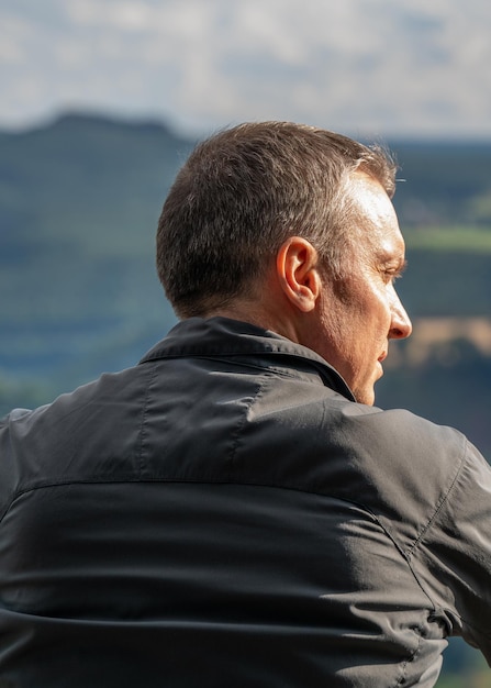 man van middelbare leeftijd zit op een berg en draait zijn rug naar de zijkant Saksisch Zwitserland Duitsland