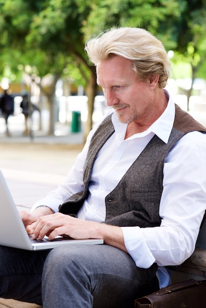 Man van middelbare leeftijd zitten buiten met behulp van laptop