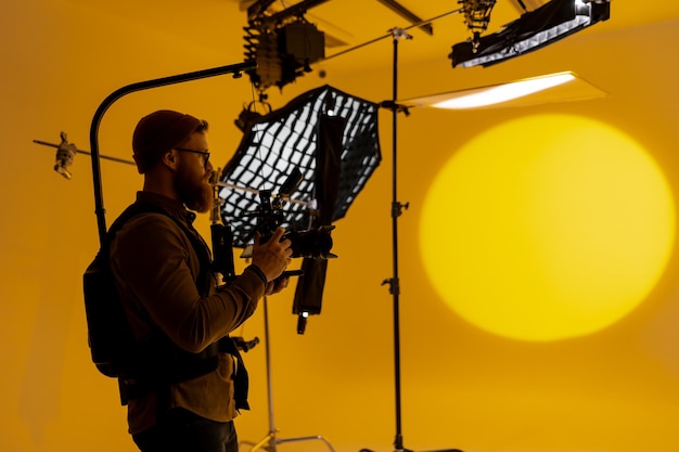 Foto man vangt grote gele achtergrond met camera in filmstudio het creëren van een silhouet tegen de