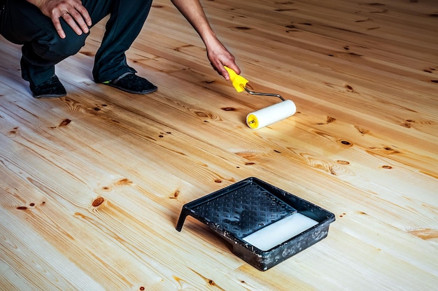 ローラーで木製の床にニスを塗る男