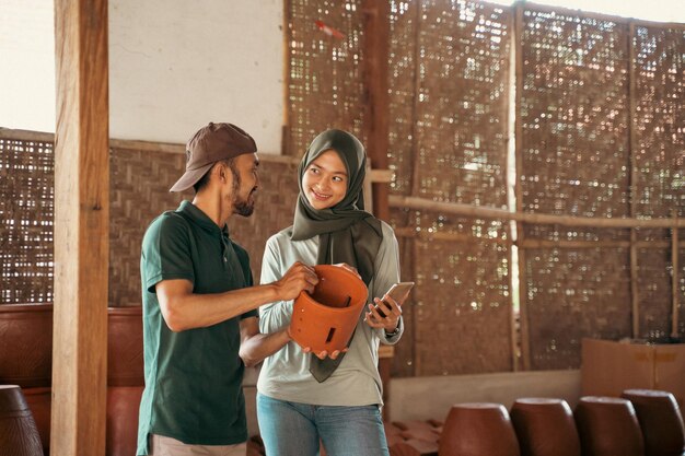 Man and veiled woman using smartphone while chatting between pottery