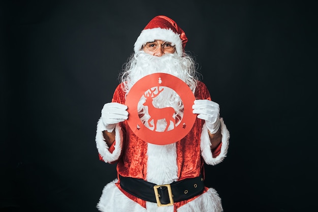 Man verkleed als kerstman met een verbiedend rendier verkeersbord, op zwarte achtergrond. Kerstconcept, Kerstman, geschenken, feest.