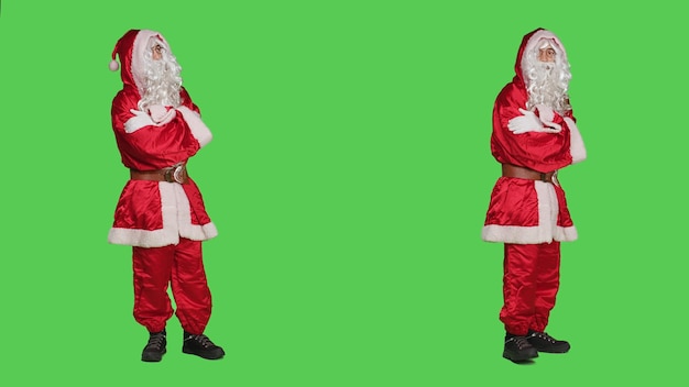 Man verkleed als kerstman voelt zich ongeduldig en wacht op iets terwijl hij over de groene achtergrond van het volledige lichaam staat. Saint Nick-personage loopt rond in de studio, kerstavondvakantie.