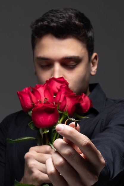 man verliefd in donkere kleding met een boeket rode rozen foto in studio grijze achtergrond