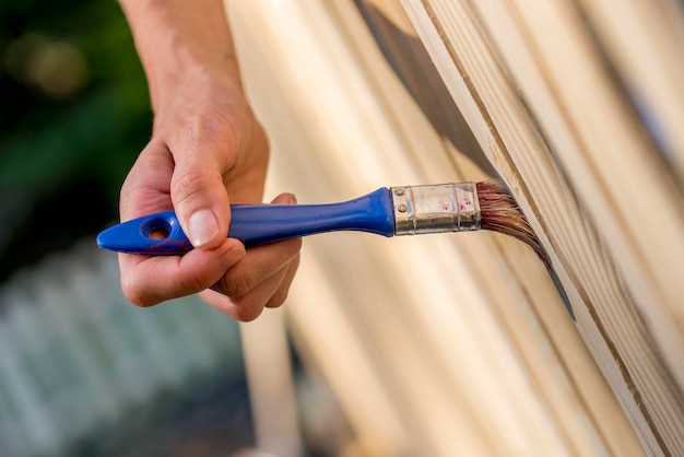 Man vernist houten hek in zijn tuin