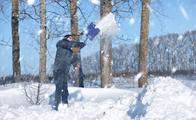 Man verwijdert sneeuw met schop van de weg in de besneeuwde winter